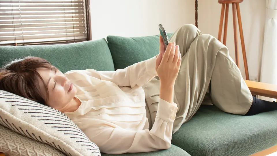 ソファに寝転がりスマートフォンを見る女性