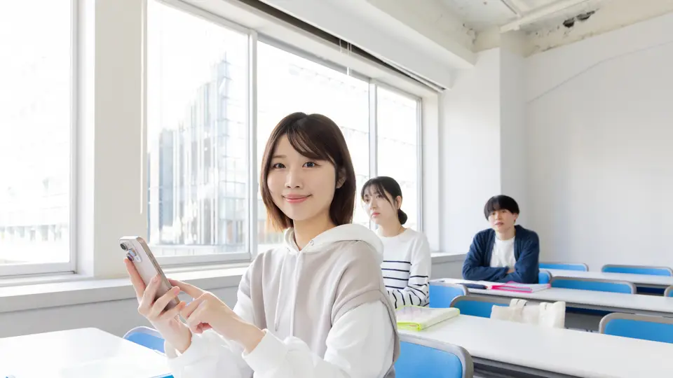 教室でスマホを見る大学生