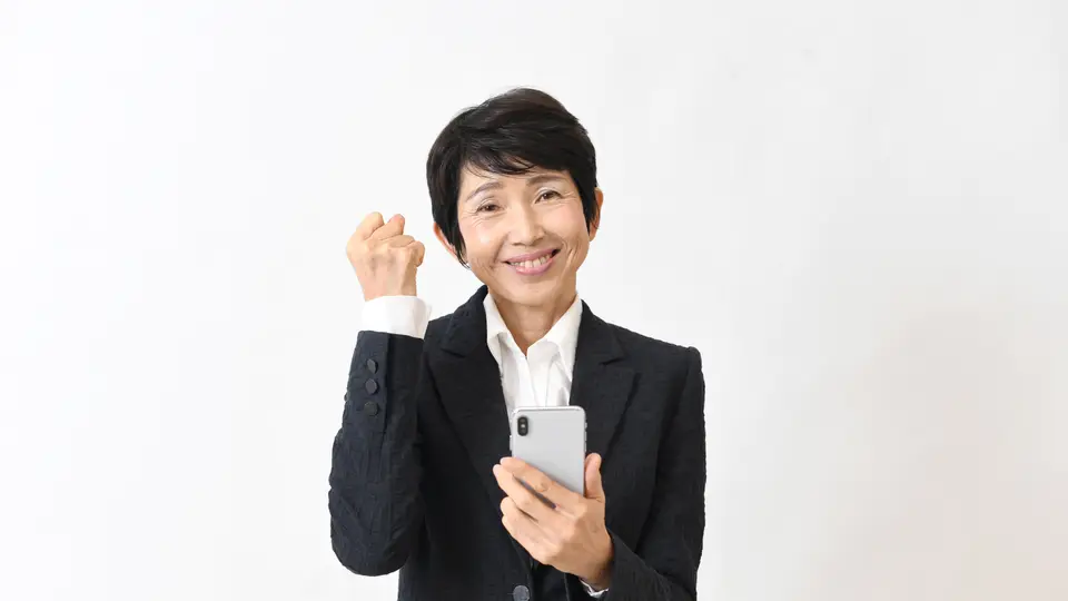 スマホを持ち喜ぶスーツ姿のシニア女性