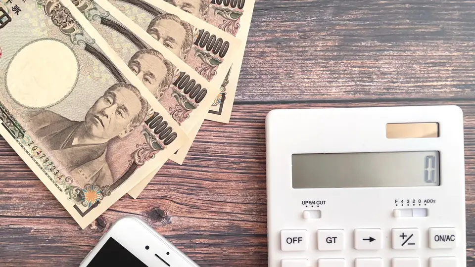 スマホとお金と電卓で計算する女性の手元