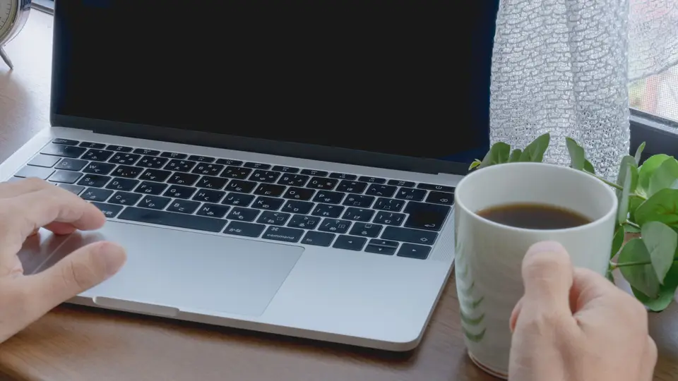 ノートパソコンを使いコーヒーを持つ手
