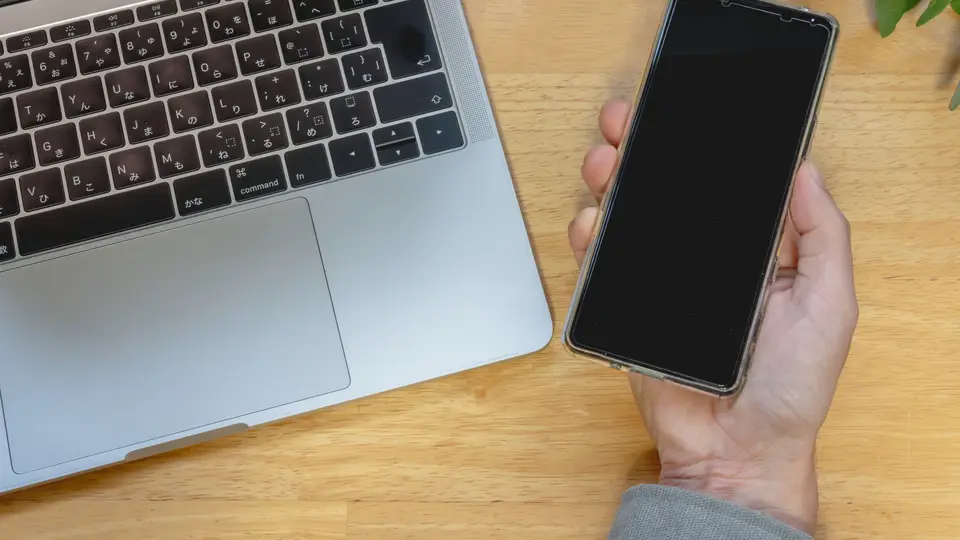 スマホを持つ手とノートパソコン