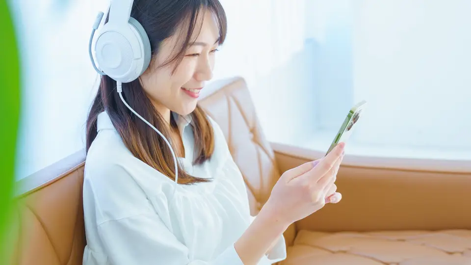 ヘッドフォンをしてスマホを見る笑顔の女性
