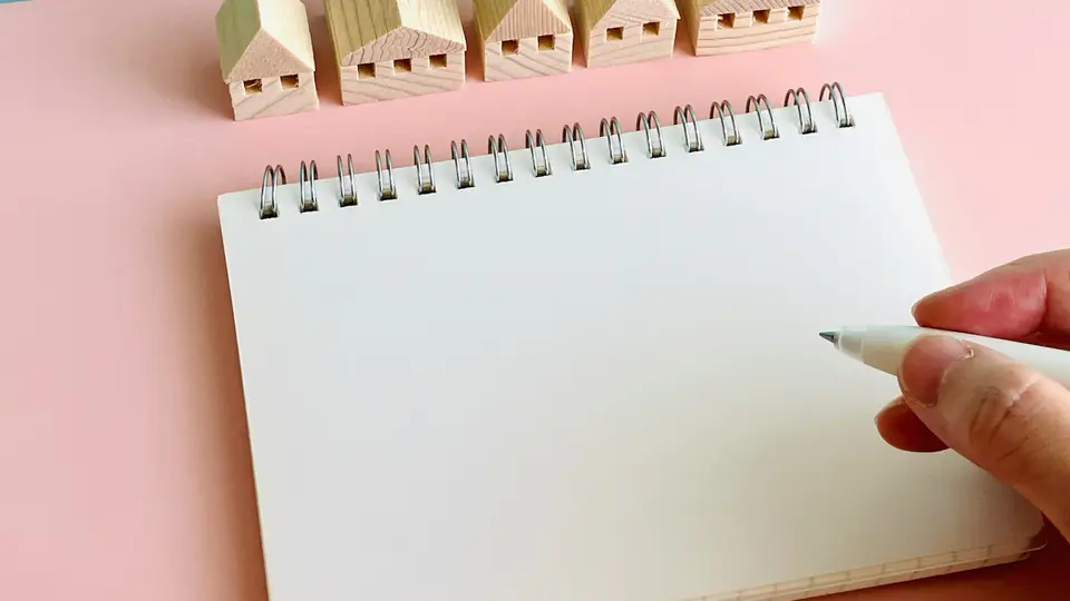 木でできた5軒の家と白紙ノートに書く手元