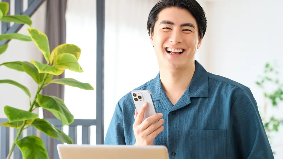 自宅でパソコンとスマホを見て笑顔の男性