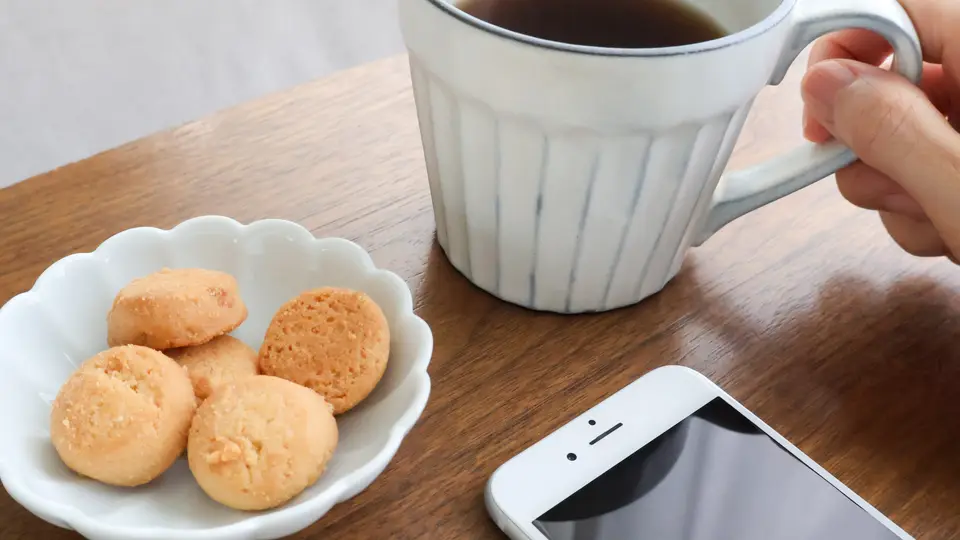 コーヒーを持つ手と机上のスマホとクッキー